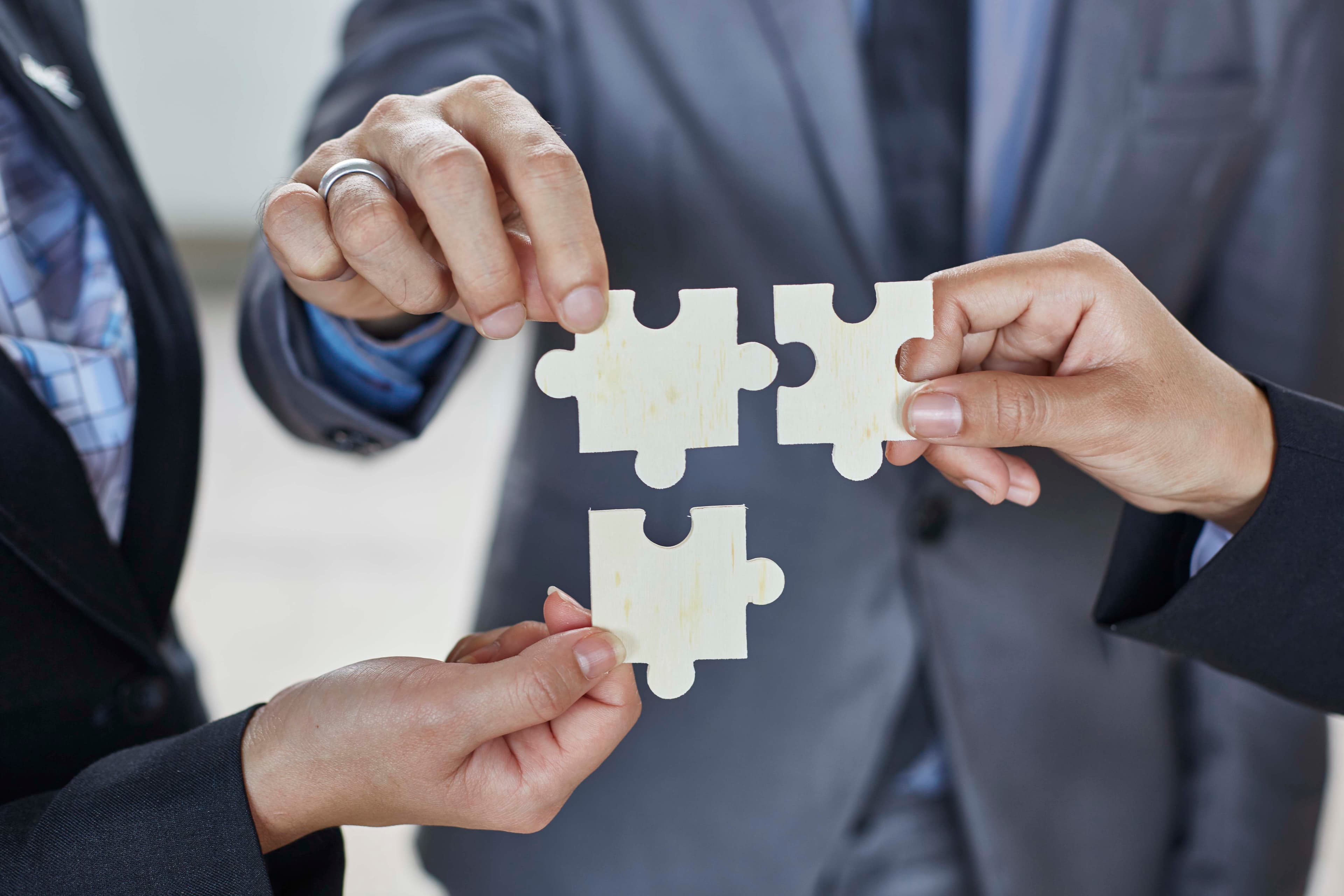 Three individuals in formal business attire each holding a piece of a puzzle, symbolizing teamwork, collaboration and problem-solving